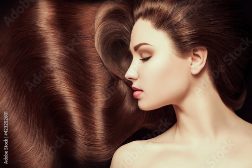 Brown Hair. Beautiful young woman with healthy luxurious long hair on dark background. Hairstyle. Hair cosmetics. Toning