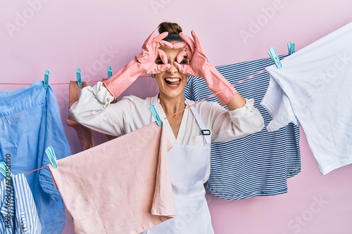 Beautiful brunette young woman washing clothes at clothesline doing ok gesture like binoculars sticking tongue out, eyes looking through fingers. crazy expression.