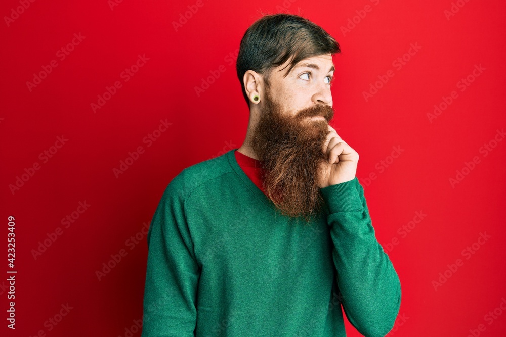 Redhead man with long beard wearing casual clothes thinking concentrated about doubt with finger on chin and looking up wondering Redhead man with long beard wearing casual clothes thinking concentrated about doubt with finger on chin and looking up wondering