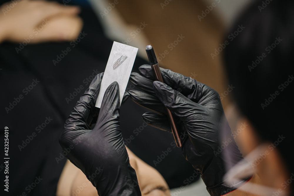microblading blending needle macro photography. A black-gloved craftsman holds a microblading needle in a package. microblading blending needle macro photography. A black-gloved craftsman holds a microblading needle in a package.