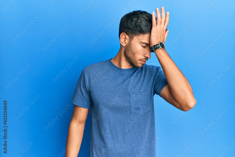 Young handsome man wearing casual tshirt over blue background surprised with hand on head for mistake, remember error. forgot, bad memory concept. Young handsome man wearing casual tshirt over blue background surprised with hand on head for mistake, remember error. forgot, bad memory concept.