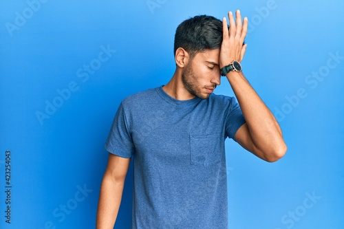 Young handsome man wearing casual tshirt over blue background surprised with hand on head for mistake, remember error. forgot, bad memory concept.