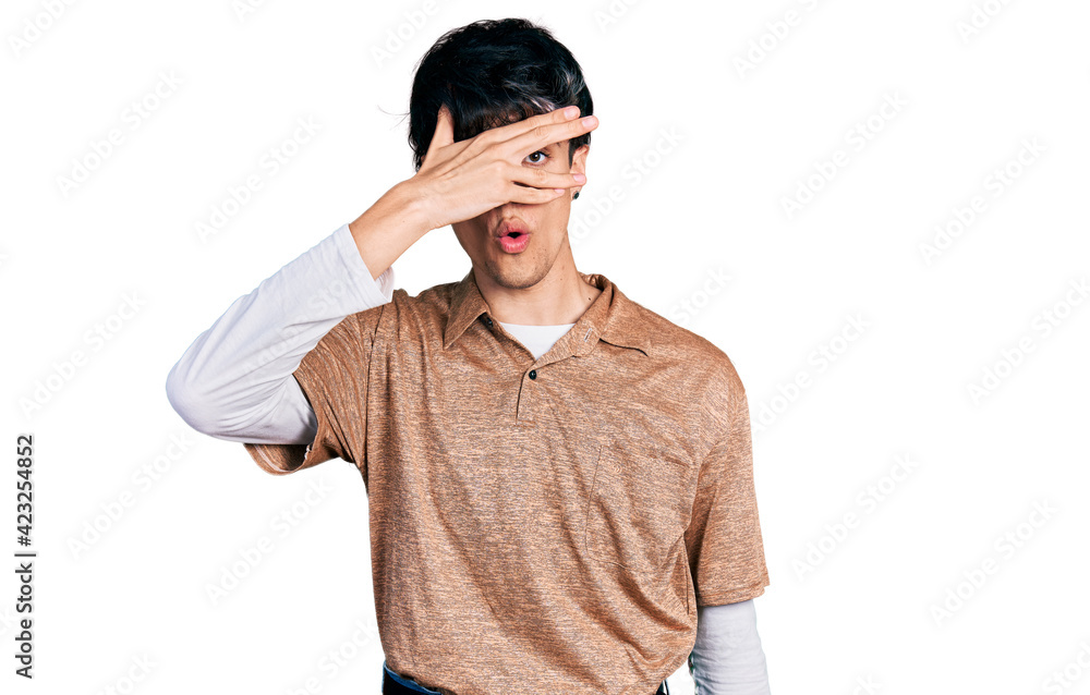 Handsome hipster young man wearing 90s retro style peeking in shock covering face and eyes with hand, looking through fingers afraid Handsome hipster young man wearing 90s retro style peeking in shock covering face and eyes with hand, looking through fingers afraid