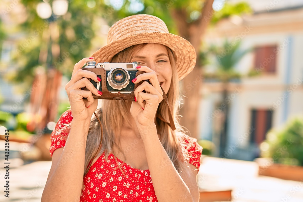 Young blonde tourist woman wearing summer style using vintage camera at the park
