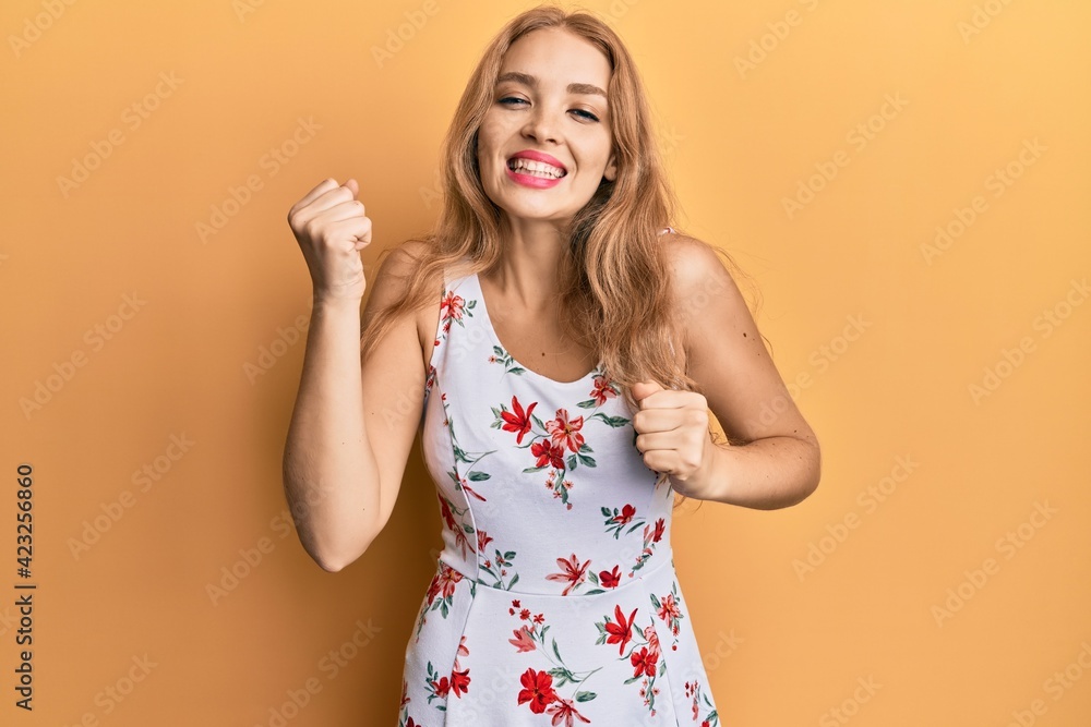 Beautiful blonde caucasian woman wearing floral dress celebrating surprised and amazed for success with arms raised and eyes closed Beautiful blonde caucasian woman wearing floral dress celebrating surprised and amazed for success with arms raised and eyes closed