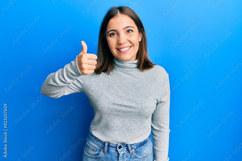 Young beautiful woman wearing casual turtleneck sweater smiling happy and positive, thumb up doing excellent and approval sign Young beautiful woman wearing casual turtleneck sweater smiling happy and positive, thumb up doing excellent and approval sign