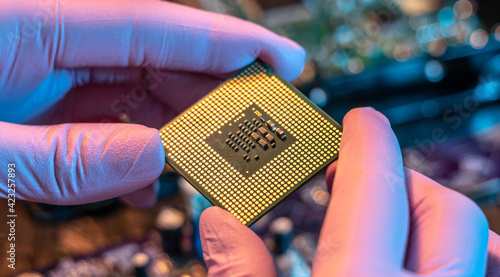 Obraz na plátně Engineer's gloved hand is holding the CPU chip on the background of the motherboard