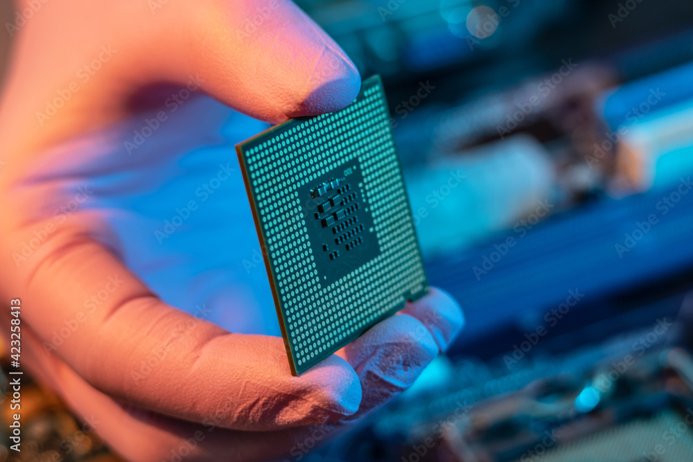 Engineer's gloved hand is holding the CPU chip on the background of the motherboard. High-tech hardware microelectronics Engineer's gloved hand is holding the CPU chip on the background of the motherboard. High-tech hardware microelectronics