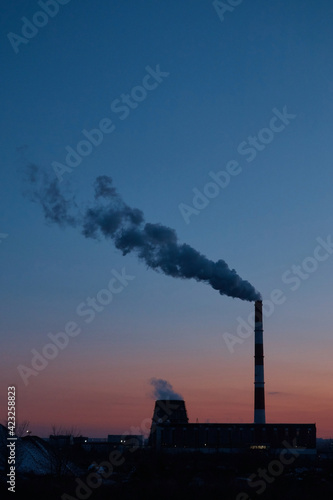 Factory from afar, steam coming from the pipe, industrial zone at sunset