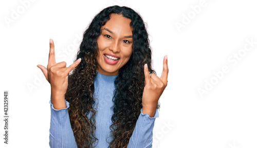 Young hispanic woman with curly hair wearing casual clothes shouting with crazy expression doing rock symbol with hands up. music star. heavy concept.