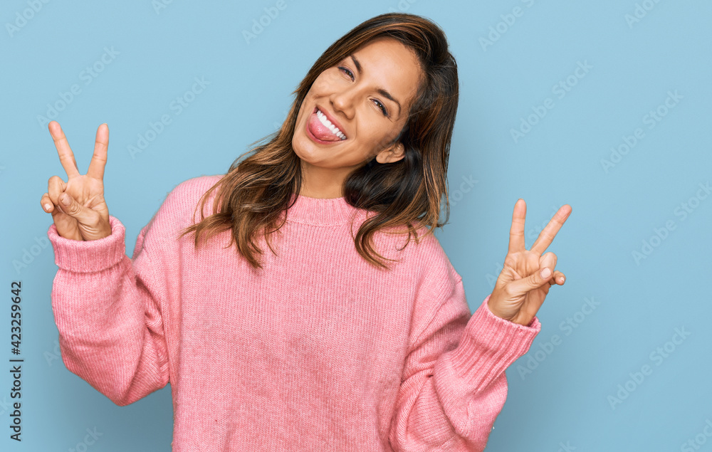 Young hispanic woman wearing casual clothes smiling with tongue out showing fingers of both hands doing victory sign. number two. Young hispanic woman wearing casual clothes smiling with tongue out showing fingers of both hands doing victory sign. number two.