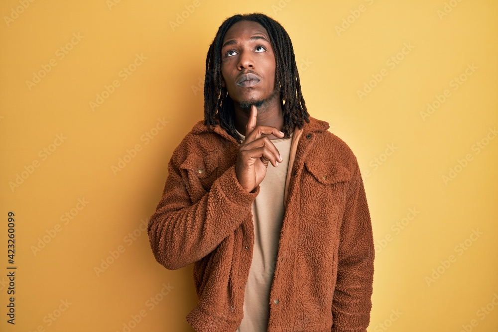African american man with braids wearing brown retro jacket thinking concentrated about doubt with finger on chin and looking up wondering African american man with braids wearing brown retro jacket thinking concentrated about doubt with finger on chin and looking up wondering