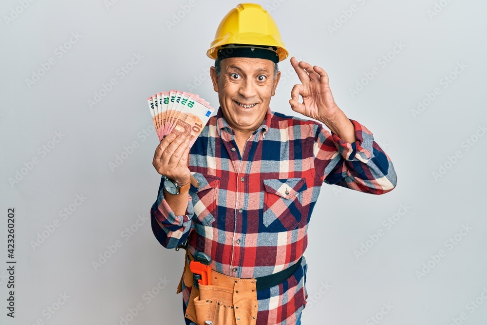 Senior hispanic man wearing handyman uniform and hardhat doing ok sign with fingers, smiling friendly gesturing excellent symbol Senior hispanic man wearing handyman uniform and hardhat doing ok sign with fingers, smiling friendly gesturing excellent symbol