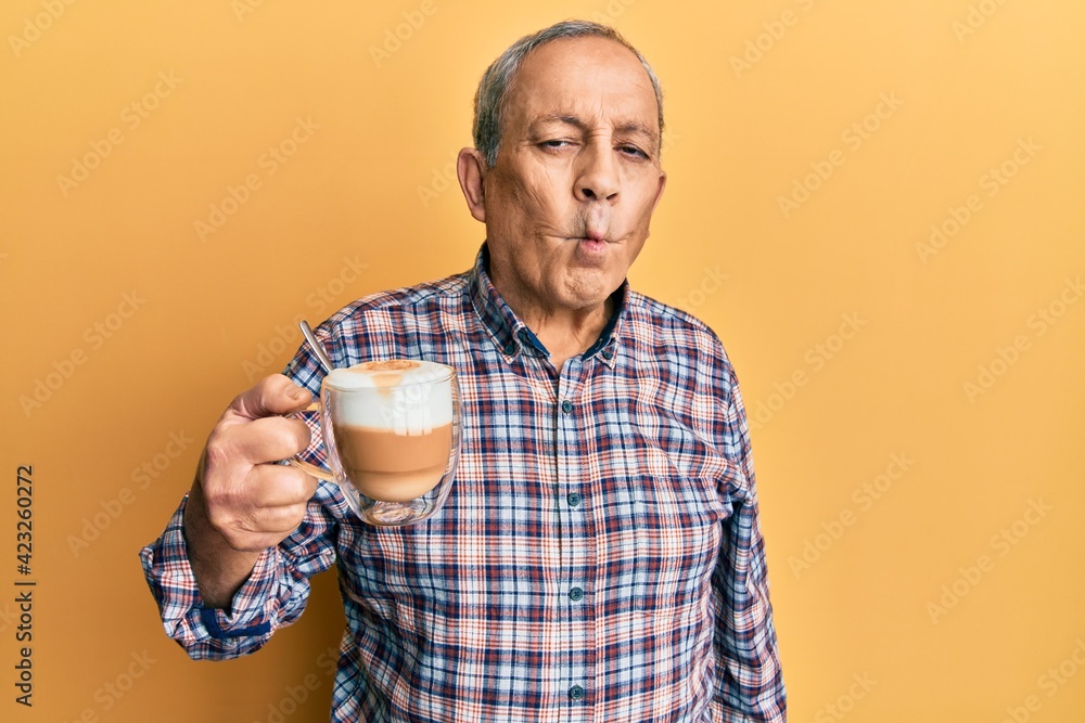 Handsome senior man with grey hair drinking a cup coffee making fish face with lips, crazy and comical gesture. funny expression. Handsome senior man with grey hair drinking a cup coffee making fish face with lips, crazy and comical gesture. funny expression.