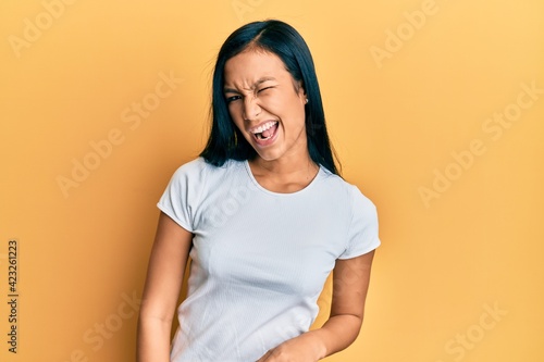 Beautiful hispanic woman wearing casual white tshirt winking looking at the camera with sexy expression, cheerful and happy face.