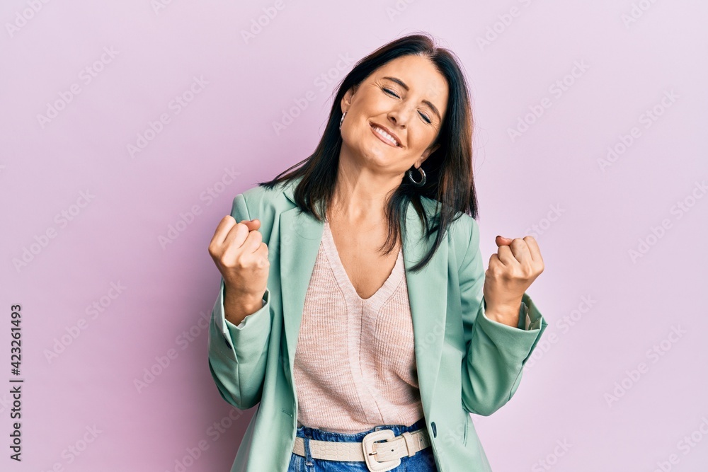 Middle age brunette woman wearing casual clothes very happy and excited doing winner gesture with arms raised, smiling and screaming for success. celebration concept. Middle age brunette woman wearing casual clothes very happy and excited doing winner gesture with arms raised, smiling and screaming for success. celebration concept.