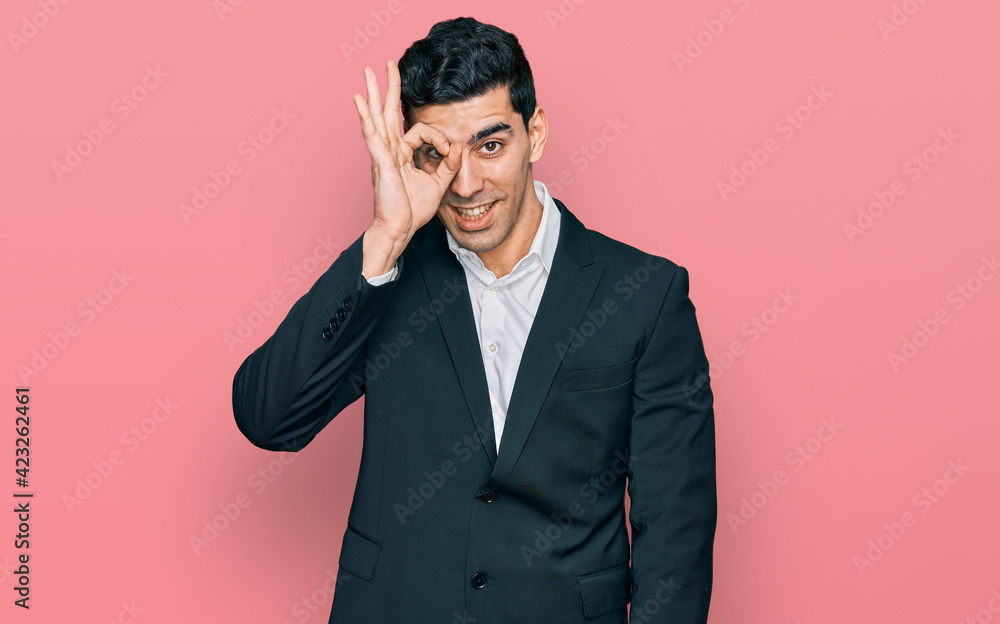 Handsome hispanic man wearing business clothes doing ok gesture with hand smiling, eye looking through fingers with happy face. Handsome hispanic man wearing business clothes doing ok gesture with hand smiling, eye looking through fingers with happy face.