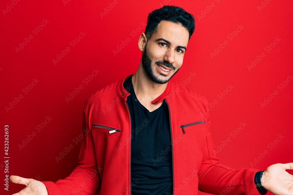 Young hispanic man wearing red leather jacket smiling showing both hands open palms, presenting and advertising comparison and balance Young hispanic man wearing red leather jacket smiling showing both hands open palms, presenting and advertising comparison and balance