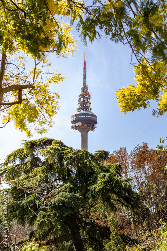 Torrespaña building, commonly known as Piruli in Madrid, surrounded by trees and yellow flowers in a sunny day during spring 