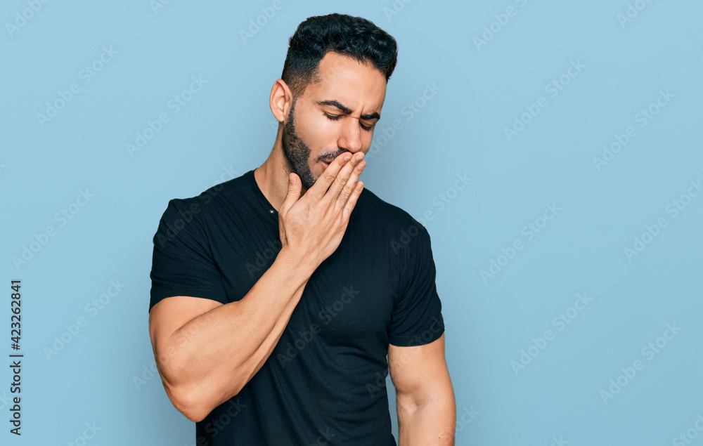 Hispanic man with beard wearing casual black t shirt bored yawning tired covering mouth with hand. restless and sleepiness. Hispanic man with beard wearing casual black t shirt bored yawning tired covering mouth with hand. restless and sleepiness.