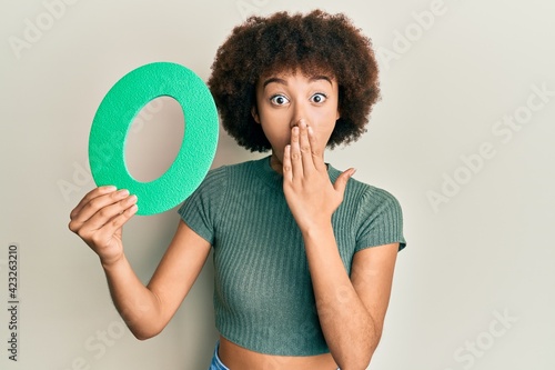 Young hispanic girl holding number zero covering mouth with hand, shocked and afraid for mistake. surprised expression photo