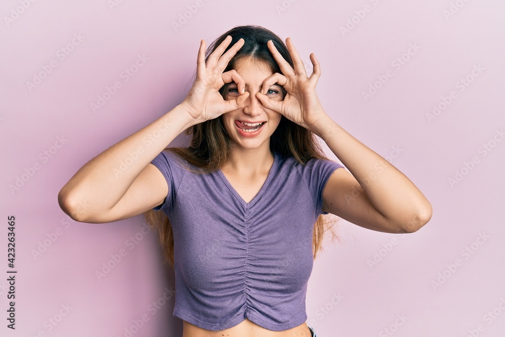 Young caucasian woman wearing casual clothes doing ok gesture like binoculars sticking tongue out, eyes looking through fingers. crazy expression.