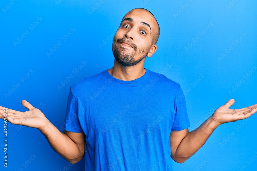 Naklejka premium Hispanic adult man wearing casual blue t shirt clueless and confused with open arms, no idea and doubtful face.