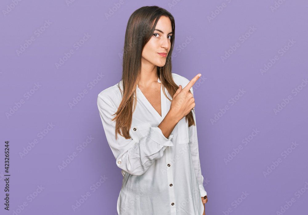 Young beautiful woman wearing casual clothes pointing with hand finger to the side showing advertisement, serious and calm face Young beautiful woman wearing casual clothes pointing with hand finger to the side showing advertisement, serious and calm face