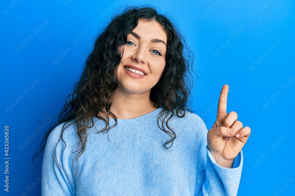 Young brunette woman with curly hair wearing casual clothes showing and pointing up with finger number one while smiling confident and happy. Young brunette woman with curly hair wearing casual clothes showing and pointing up with finger number one while smiling confident and happy.