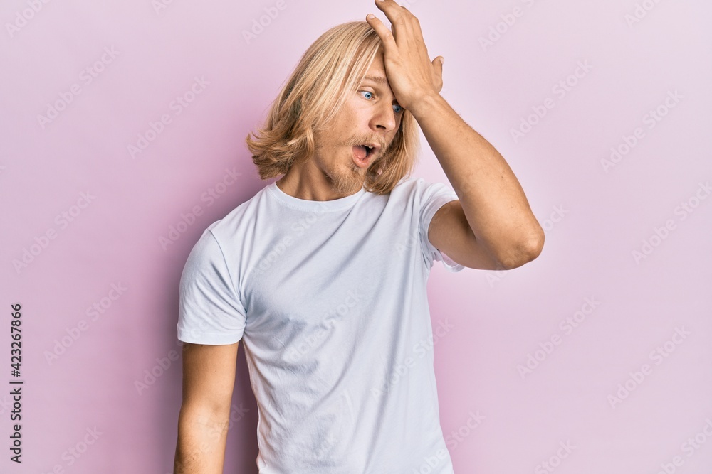 Caucasian young man with long hair wearing casual white t shirt surprised with hand on head for mistake, remember error. forgot, bad memory concept. Caucasian young man with long hair wearing casual white t shirt surprised with hand on head for mistake, remember error. forgot, bad memory concept.