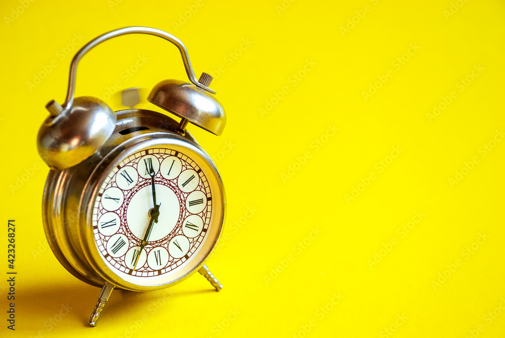 The old alarm clock rings on an isolated yellow background.