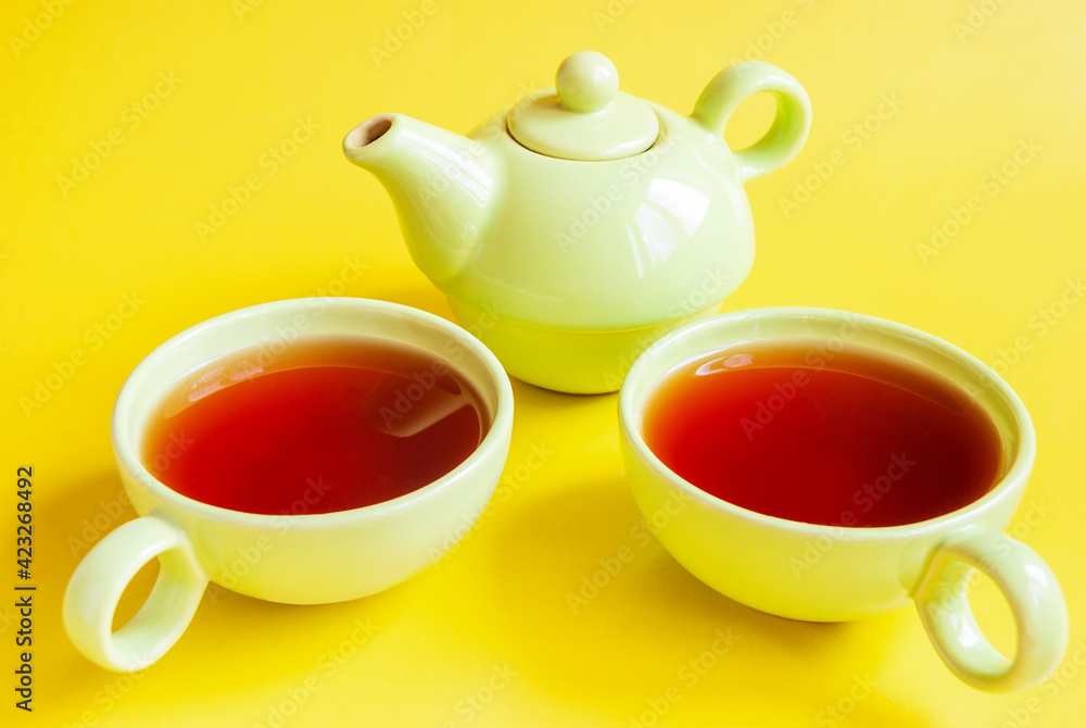 A green tea service made of teapot and two mugs with tea on an isolated yellow background. A green tea service made of teapot and two mugs with tea on an isolated yellow background.