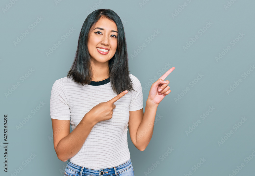 Beautiful asian young woman wearing casual white t shirt smiling and looking at the camera pointing with two hands and fingers to the side. Beautiful asian young woman wearing casual white t shirt smiling and looking at the camera pointing with two hands and fingers to the side.
