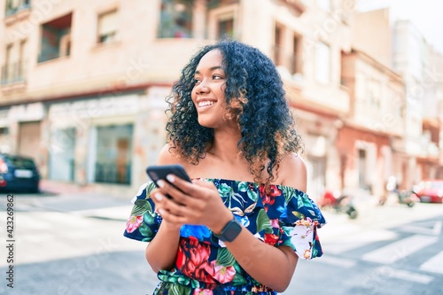 Young african american woman with curly hair smiling happy outdoors using smartphone