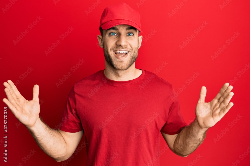 Young caucasian man wearing delivery uniform and cap celebrating victory with happy smile and winner expression with raised hands Young caucasian man wearing delivery uniform and cap celebrating victory with happy smile and winner expression with raised hands