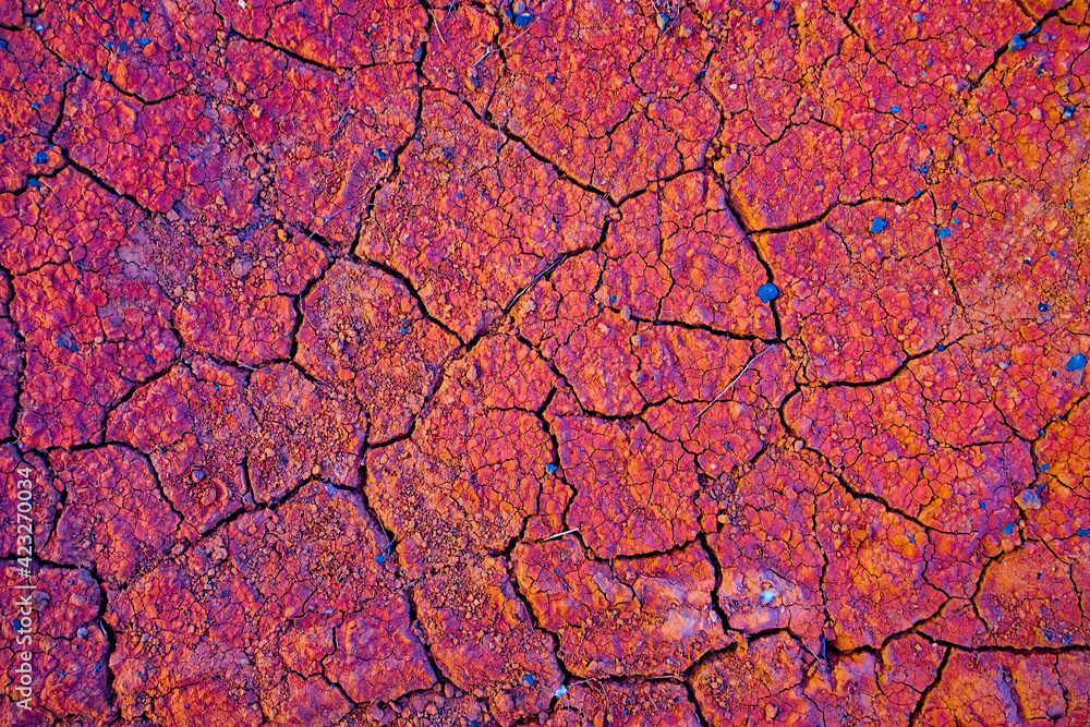 Fototapeta premium Rusty red cracked soil rich in iron ore, extremely warm sunset light, small lava stones and pebbles.