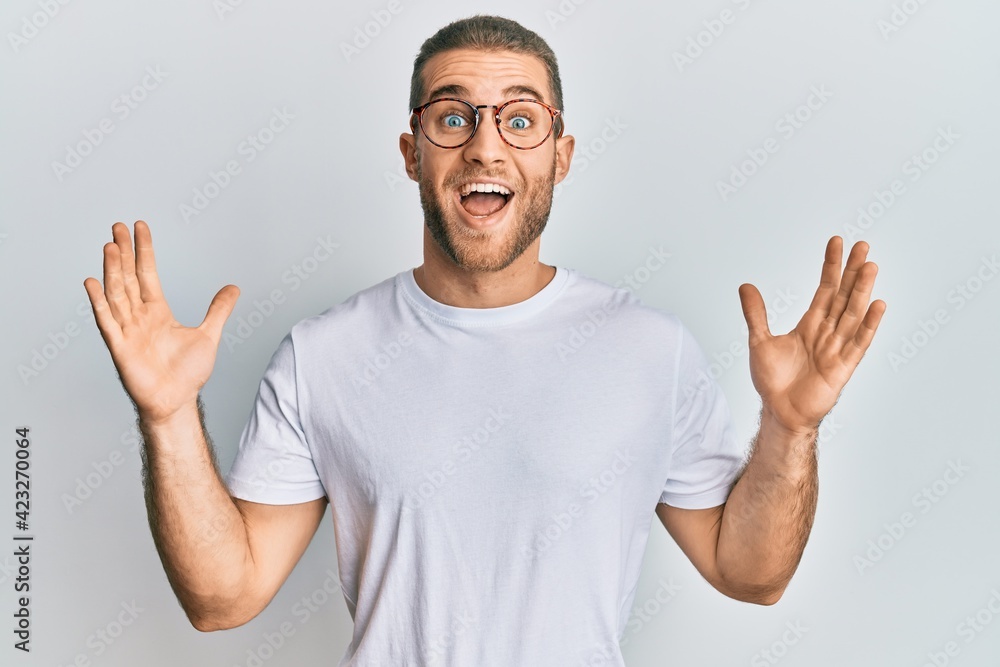 Young caucasian man wearing casual clothes and glasses celebrating crazy and amazed for success with arms raised and open eyes screaming excited. winner concept Young caucasian man wearing casual clothes and glasses celebrating crazy and amazed for success with arms raised and open eyes screaming excited. winner concept