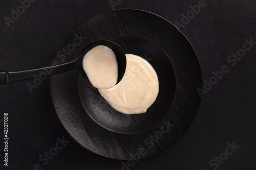 Cream soup in black plate over dark background from above.
