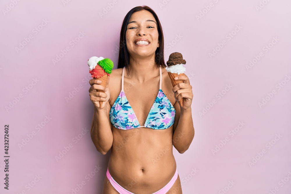 Naklejka premium Young latin woman wearing bikini holding ice cream smiling with a happy and cool smile on face. showing teeth.