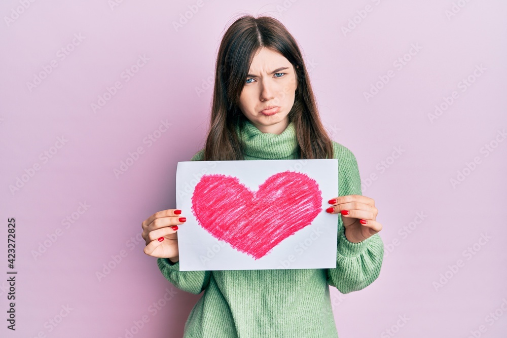 Young beautiful caucasian girl holding heart draw depressed and worry for distress, crying angry and afraid. sad expression. Young beautiful caucasian girl holding heart draw depressed and worry for distress, crying angry and afraid. sad expression.