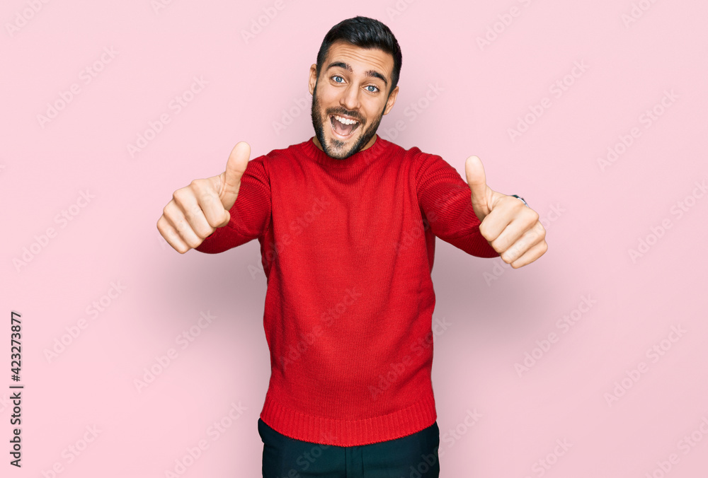 Naklejka premium Young hispanic man wearing casual clothes approving doing positive gesture with hand, thumbs up smiling and happy for success. winner gesture.