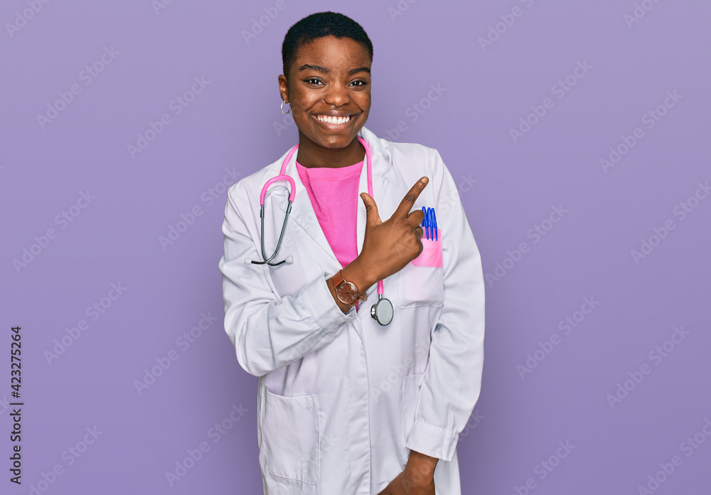 Young african american woman wearing doctor uniform and stethoscope cheerful with a smile of face pointing with hand and finger up to the side with happy and natural expression on face Young african american woman wearing doctor uniform and stethoscope cheerful with a smile of face pointing with hand and finger up to the side with happy and natural expression on face