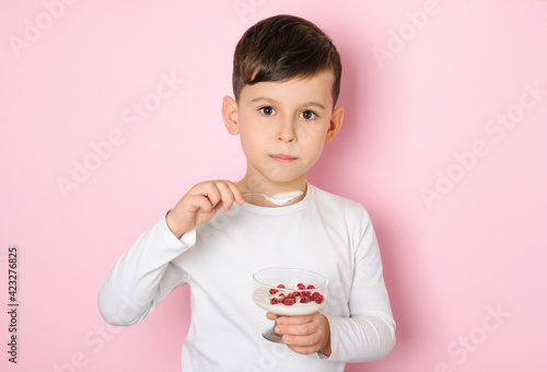 Little boy 6 years old eating yogurt with red berries on a pink background. Healthy kids food