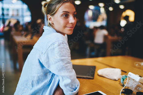 Carefree female dressed in comfort linen shirt sitting at cafeteria table and thinking about ideas, thoughtful Caucasian hipster girl in casual clothing feeling pondering during leisure in coworking