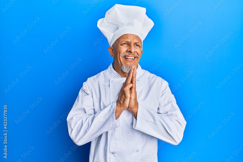 Middle age grey-haired man wearing professional cook uniform and hat begging and praying with hands together with hope expression on face very emotional and worried. begging. Middle age grey-haired man wearing professional cook uniform and hat begging and praying with hands together with hope expression on face very emotional and worried. begging.