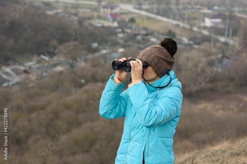 Girl looking through binoculars while standing on top of a mountain on a warm autumn day