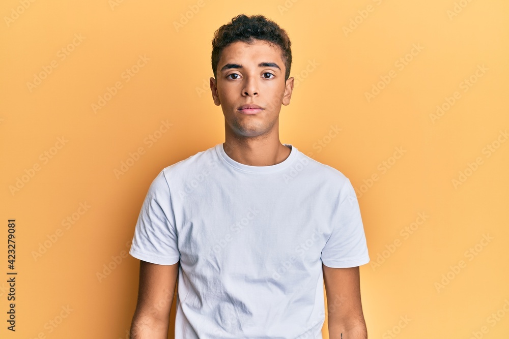Young handsome african american man wearing casual white tshirt with serious expression on face. simple and natural looking at the camera. Young handsome african american man wearing casual white tshirt with serious expression on face. simple and natural looking at the camera.