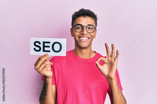 Obraz na plátně Young handsome african american man holding seo message paper doing ok sign with