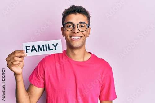 Fototapet Young handsome african american man holding family paper looking positive and ha