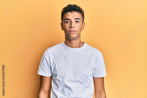 Young handsome african american man wearing casual white tshirt with serious expression on face. simple and natural looking at the camera.